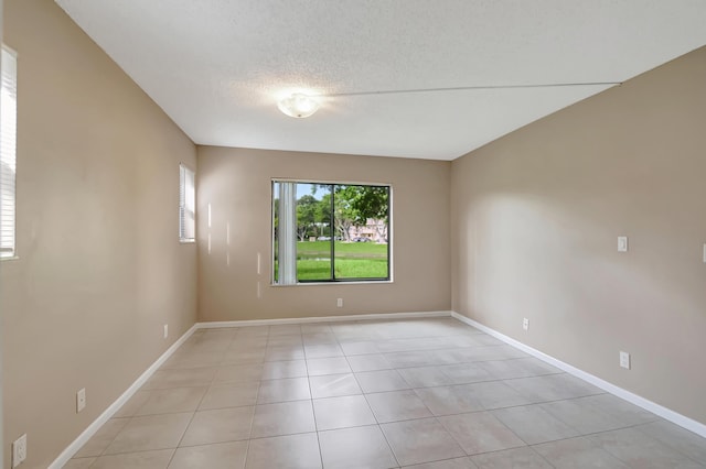 empty room with a textured ceiling, light tile patterned floors, and baseboards