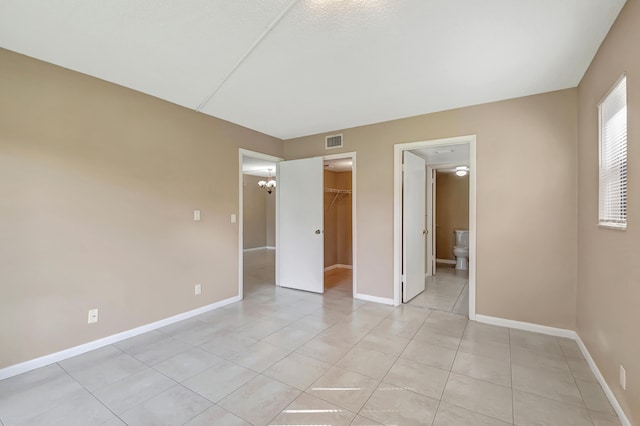 unfurnished bedroom featuring a closet, connected bathroom, a walk in closet, and light tile patterned floors