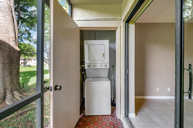 laundry room featuring plenty of natural light, stacked washer and clothes dryer, and dark tile patterned flooring