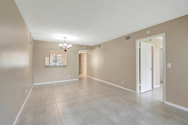 empty room with light tile patterned floors, a notable chandelier, and a textured ceiling