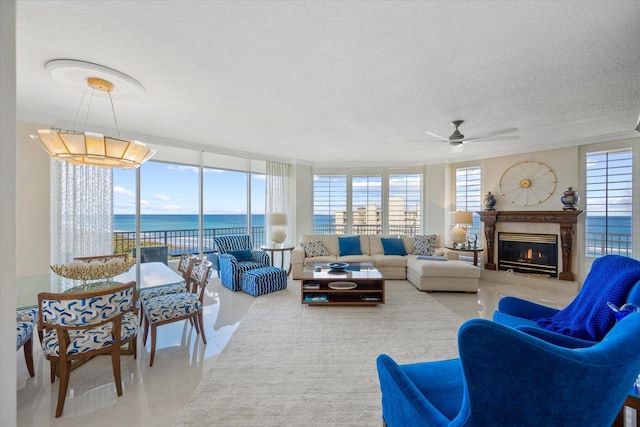 tiled living room featuring a fireplace, ceiling fan, floor to ceiling windows, a water view, and a textured ceiling