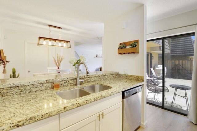 kitchen featuring light wood-type flooring, pendant lighting, dishwasher, sink, and light stone countertops