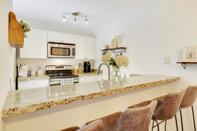 kitchen with appliances with stainless steel finishes, a kitchen bar, kitchen peninsula, light stone counters, and white cabinets