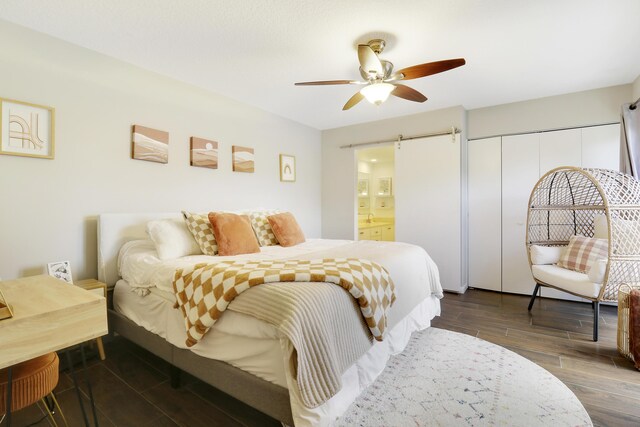 bedroom featuring dark wood-type flooring, ceiling fan, a barn door, and ensuite bathroom