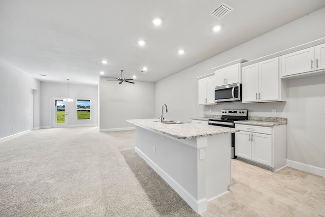 kitchen with light carpet, stainless steel appliances, ceiling fan, a center island with sink, and white cabinets