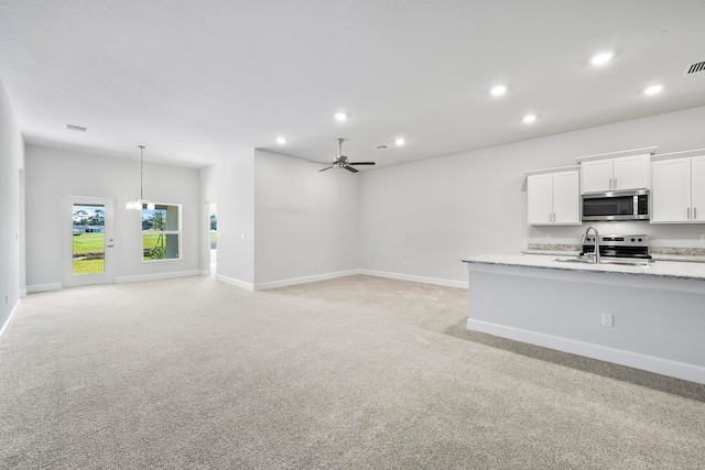 kitchen featuring ceiling fan with notable chandelier, stainless steel appliances, white cabinetry, and light colored carpet