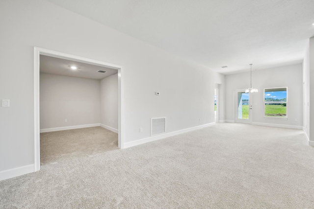 carpeted spare room featuring an inviting chandelier