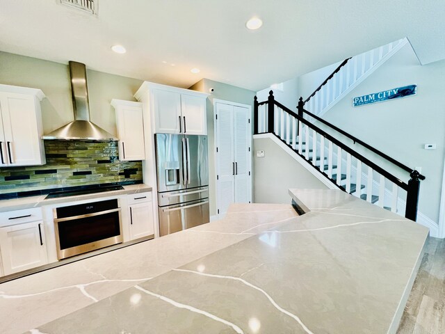 kitchen with appliances with stainless steel finishes, wall chimney exhaust hood, white cabinets, and light stone counters