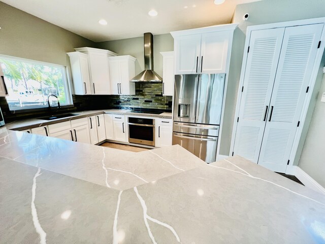 kitchen featuring appliances with stainless steel finishes, white cabinetry, sink, backsplash, and wall chimney range hood