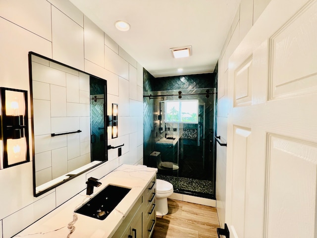 bathroom with toilet, vanity, tile walls, hardwood / wood-style flooring, and a shower with shower door