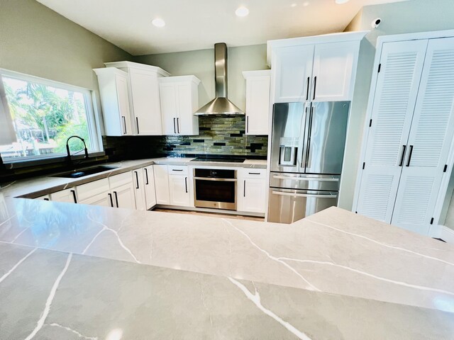 kitchen with stainless steel fridge, backsplash, wall chimney exhaust hood, white cabinets, and sink