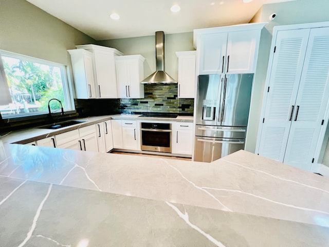 kitchen featuring wall chimney exhaust hood, sink, stainless steel appliances, and white cabinetry