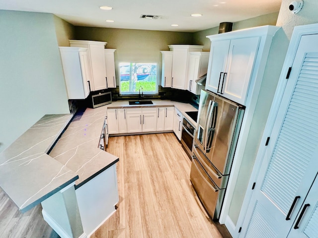 kitchen with decorative backsplash, sink, light wood-type flooring, stainless steel appliances, and white cabinets