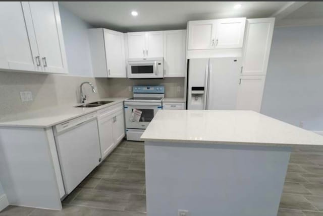 kitchen with white appliances, a center island, white cabinetry, and sink