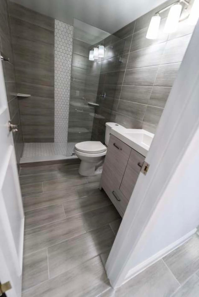 bathroom with a tile shower, tile walls, vanity, and toilet