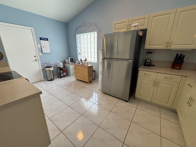 kitchen with lofted ceiling, cream cabinetry, light tile patterned floors, and stainless steel refrigerator