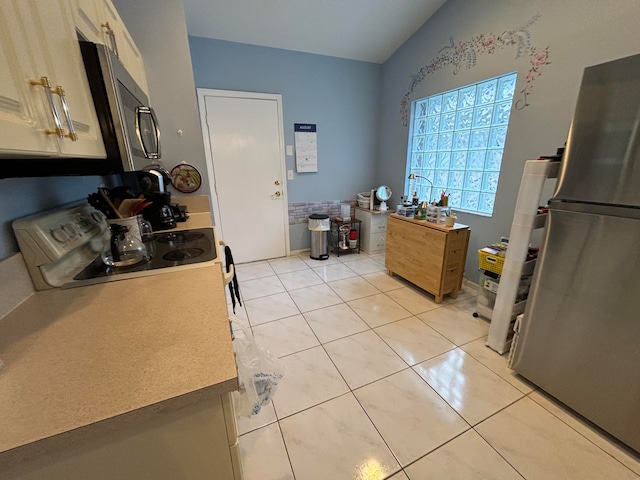 kitchen with stainless steel appliances, lofted ceiling, light tile patterned floors, and light brown cabinets