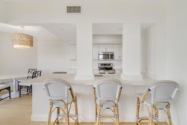 kitchen with white cabinets, light hardwood / wood-style flooring, stainless steel appliances, kitchen peninsula, and a kitchen breakfast bar