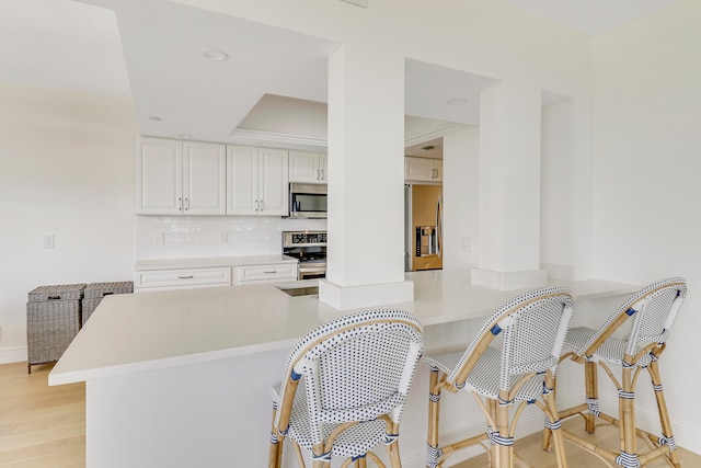 kitchen with white cabinetry, tasteful backsplash, light hardwood / wood-style flooring, kitchen peninsula, and appliances with stainless steel finishes