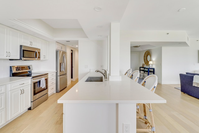 kitchen with a breakfast bar area, light hardwood / wood-style floors, stainless steel appliances, sink, and white cabinetry