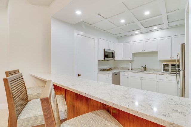 kitchen with coffered ceiling, kitchen peninsula, sink, appliances with stainless steel finishes, and a breakfast bar area