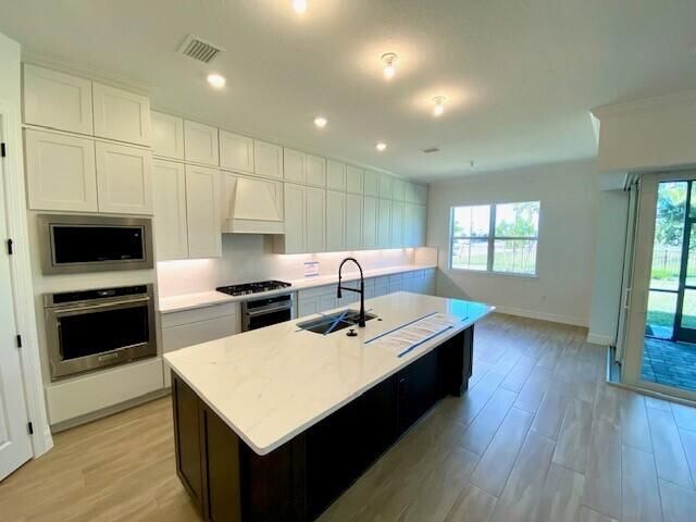 kitchen featuring white cabinets, appliances with stainless steel finishes, custom exhaust hood, light countertops, and a sink