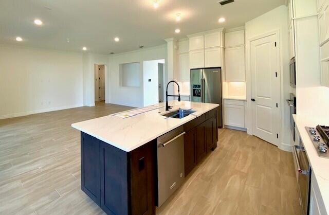 kitchen with recessed lighting, appliances with stainless steel finishes, light wood-style floors, a kitchen island with sink, and a sink