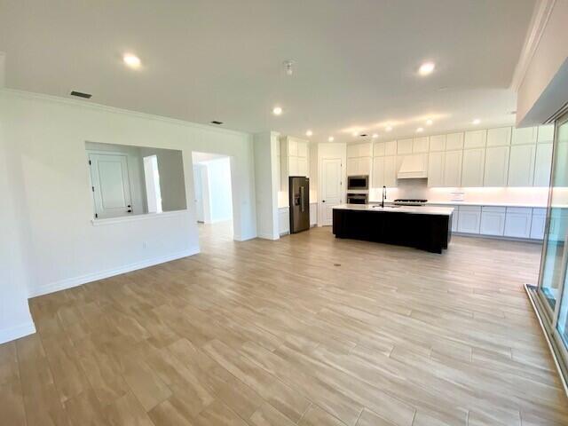 kitchen featuring black refrigerator with ice dispenser, open floor plan, a kitchen island with sink, a sink, and white cabinets