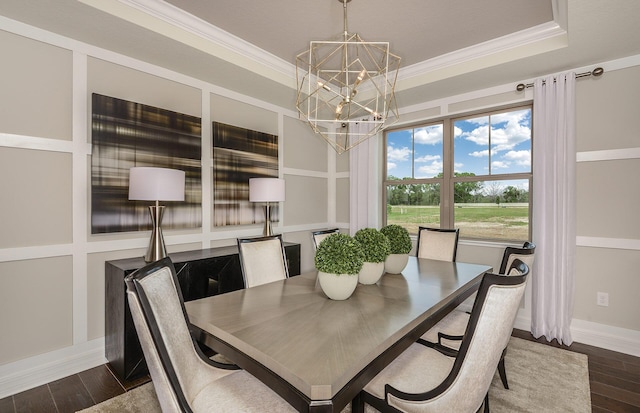 dining space with a tray ceiling, dark wood-style flooring, crown molding, and an inviting chandelier