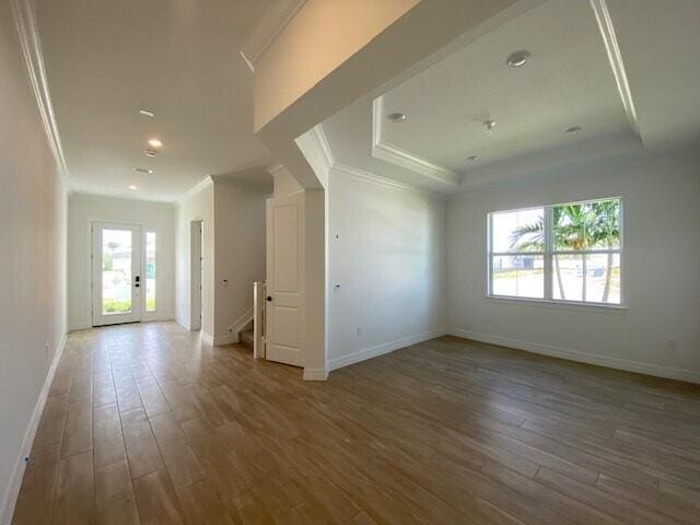 empty room with baseboards, crown molding, a tray ceiling, and dark wood-type flooring