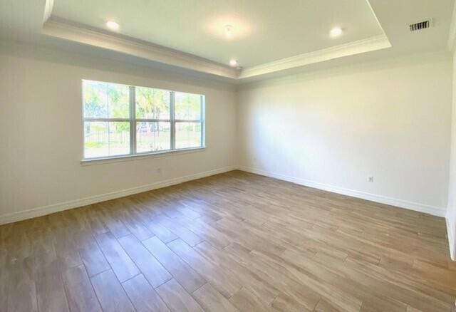 empty room with crown molding, a raised ceiling, and light wood-style floors