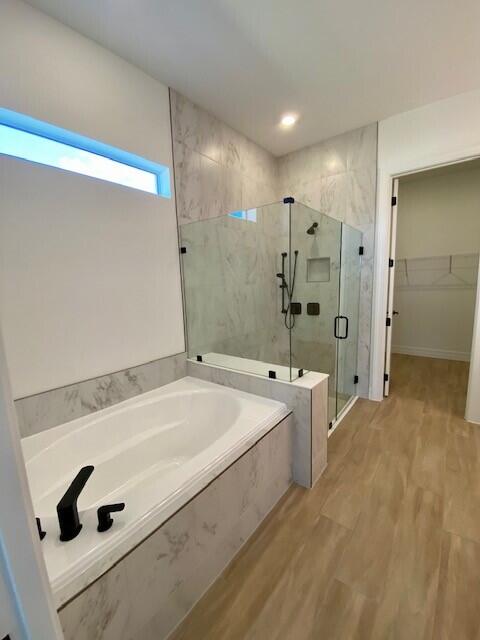 full bath featuring a garden tub, wood finished floors, a walk in closet, and a marble finish shower