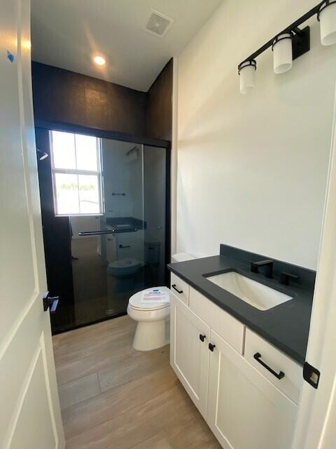 full bath featuring toilet, wood finished floors, visible vents, vanity, and a shower stall