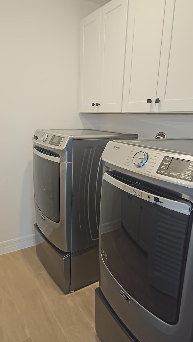 clothes washing area featuring washer and clothes dryer, light wood-type flooring, cabinet space, and baseboards