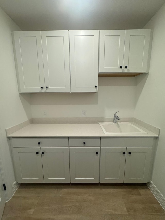 interior space featuring light countertops, white cabinets, a sink, wood finished floors, and baseboards