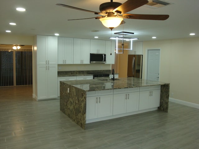 kitchen with stainless steel appliances, ceiling fan, white cabinets, and an island with sink