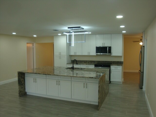 kitchen with appliances with stainless steel finishes, white cabinetry, an island with sink, and sink