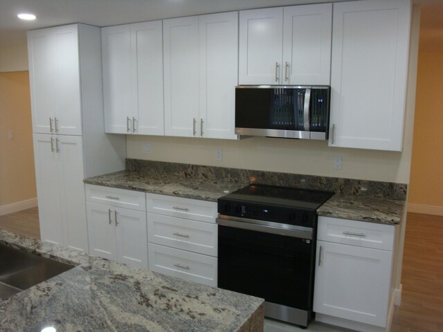 kitchen featuring light stone countertops, range, wood-type flooring, and white cabinets