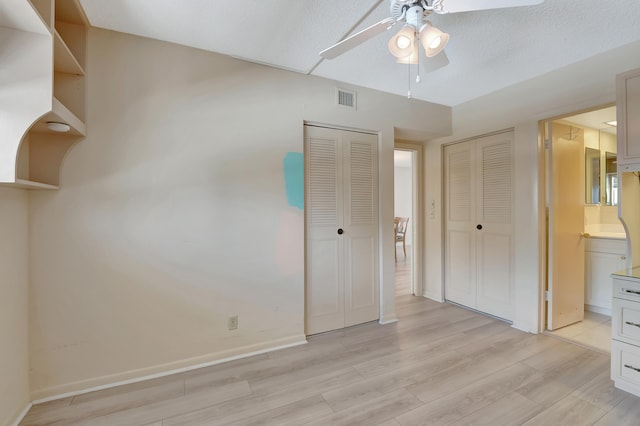 unfurnished bedroom with light wood-type flooring, a textured ceiling, ensuite bath, and ceiling fan