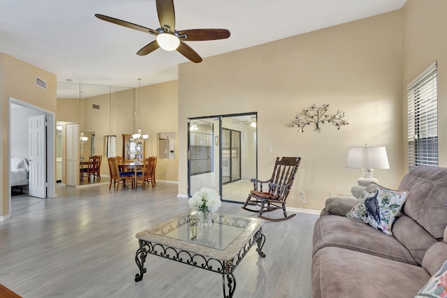 living room featuring ceiling fan, a high ceiling, and light hardwood / wood-style flooring