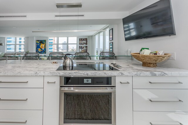 kitchen featuring light stone counters, black electric cooktop, white cabinetry, and oven