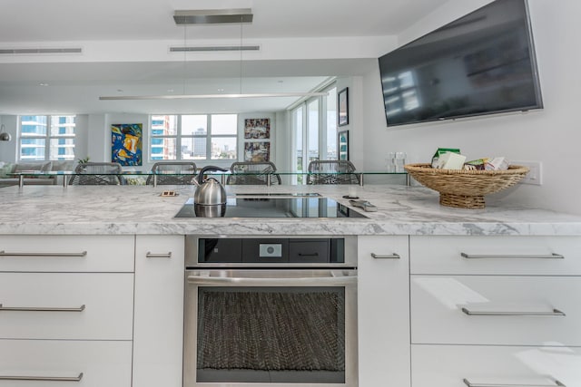 kitchen with black electric stovetop, light stone counters, white cabinets, and oven