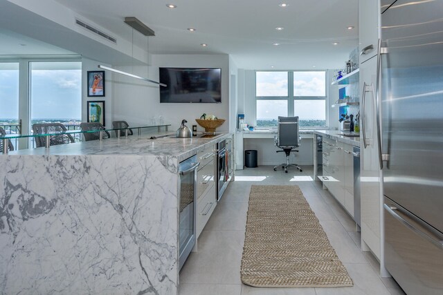 kitchen featuring light stone counters, expansive windows, light tile patterned floors, stainless steel appliances, and white cabinets