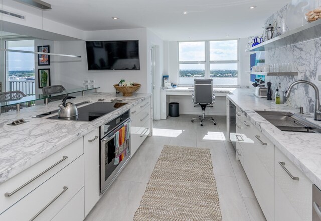 kitchen with oven, tasteful backsplash, white cabinets, light tile patterned floors, and sink