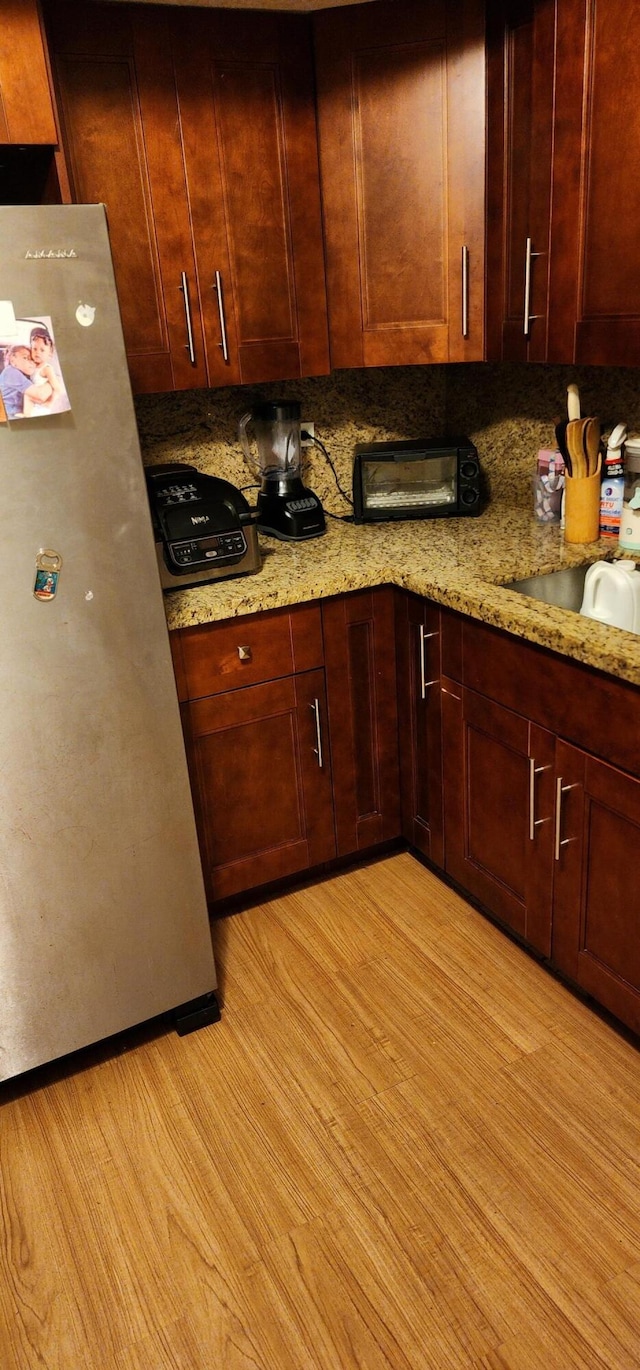 kitchen with sink, light stone counters, light hardwood / wood-style floors, tasteful backsplash, and stainless steel fridge