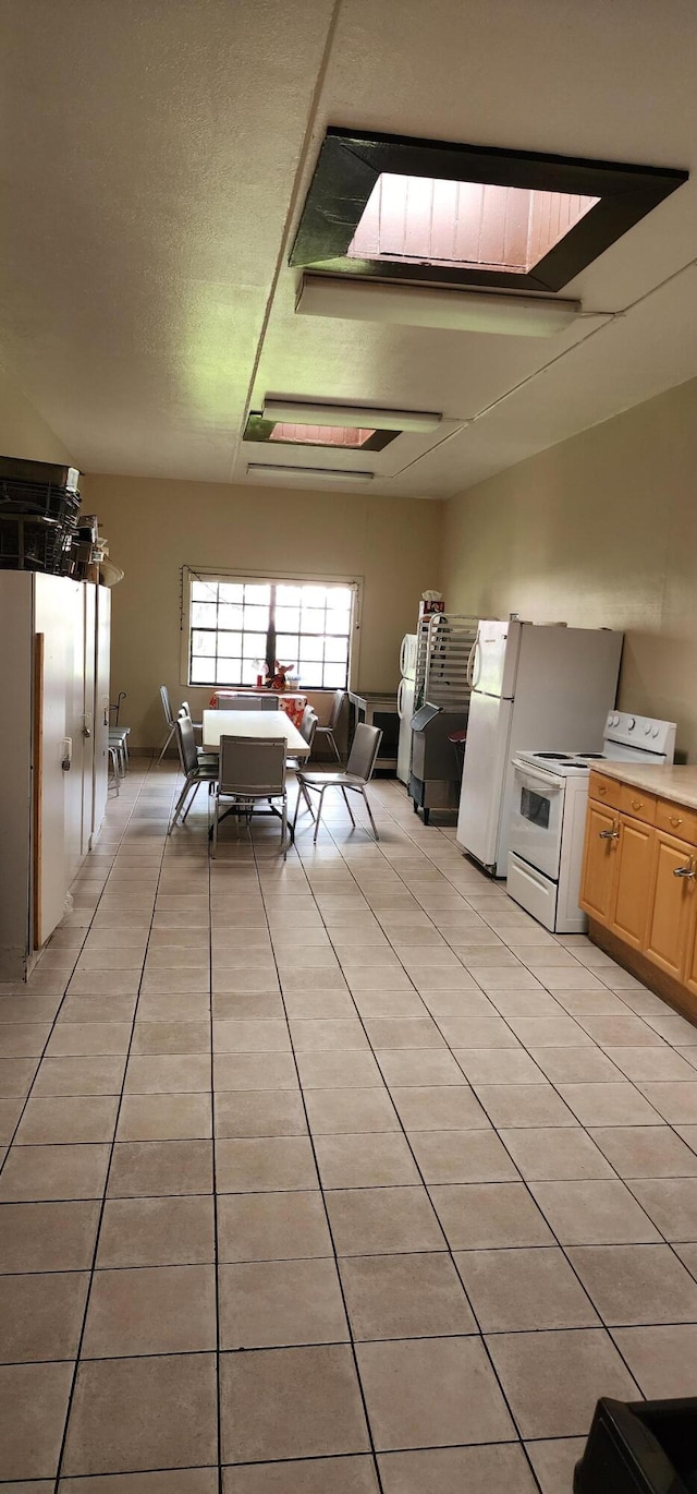 kitchen with a skylight, white appliances, and light tile patterned floors