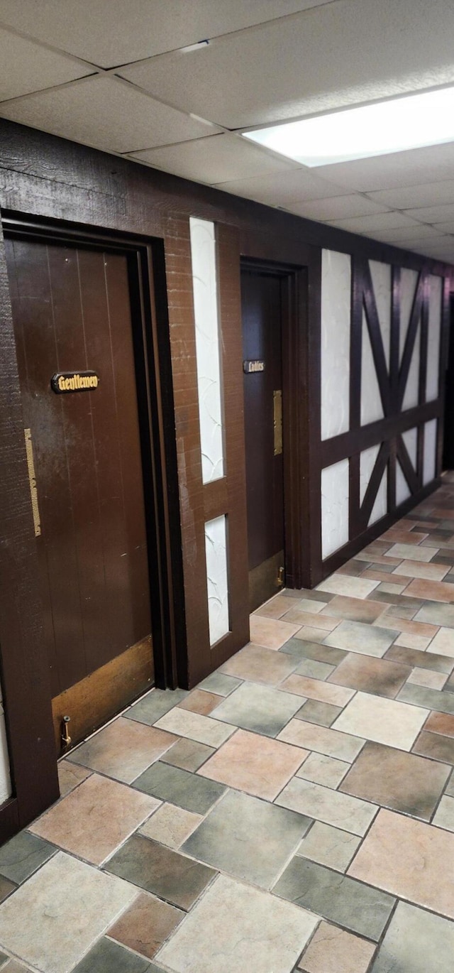 hall with light tile patterned flooring and a paneled ceiling