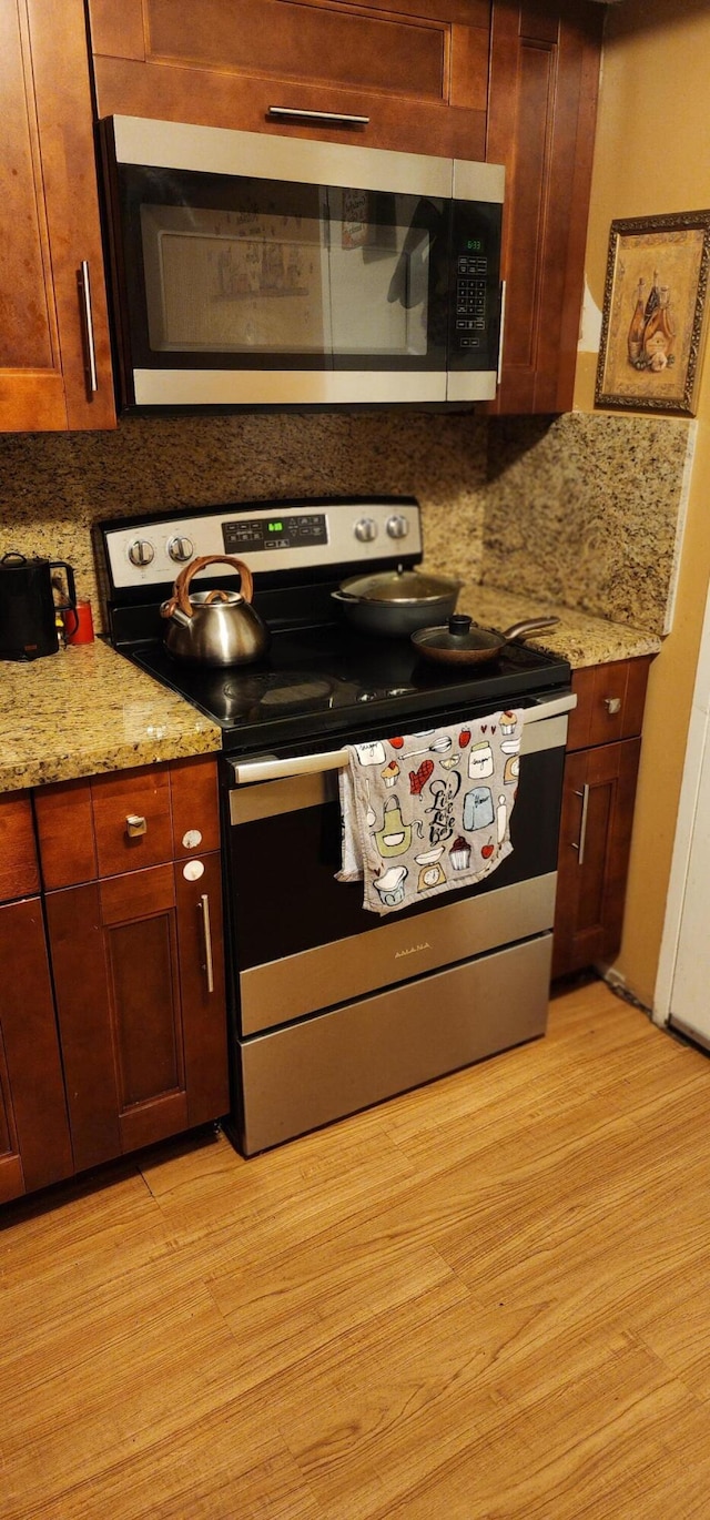 kitchen featuring appliances with stainless steel finishes, light stone countertops, light wood-type flooring, and backsplash