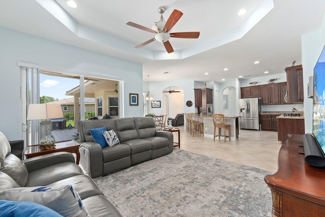 tiled living room with ceiling fan and a raised ceiling