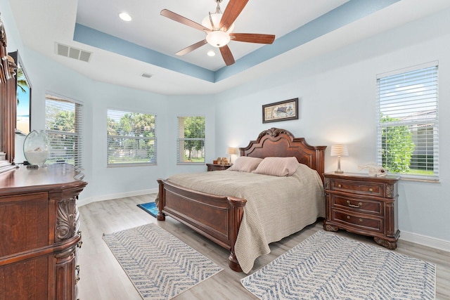 bedroom featuring ceiling fan, a raised ceiling, and light hardwood / wood-style floors